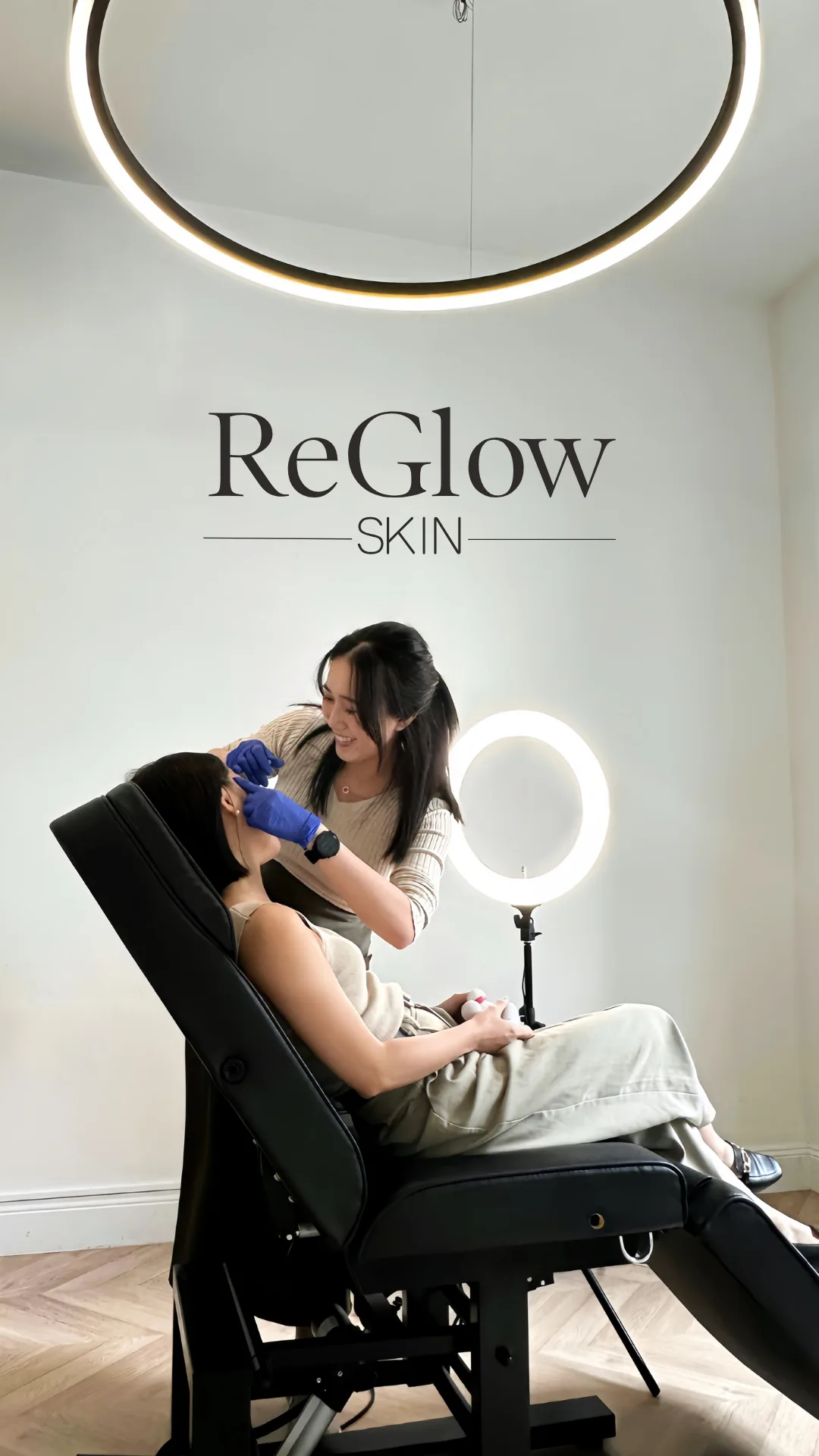 A ReGlow Skin nurse treating a reclined client beneath the clinic&rsquo;s ring light, with the ReGlow Skin logo on the wall behind them